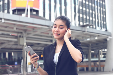 Relaxed young Asian woman listening music with mobile smart phone in urban city.