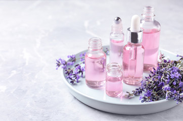 Tray with bottles of lavender essential oil and flowers on marble table. Space for text