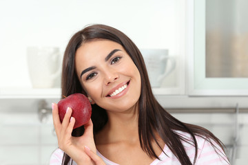 Happy woman holding fresh apple in kitchen