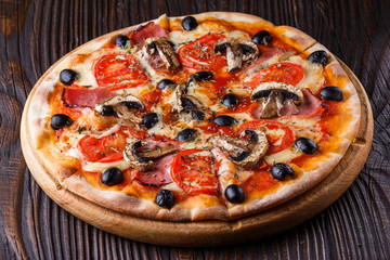 Pizza with tomato, olives, champignons, ham and cheese on round wooden plate