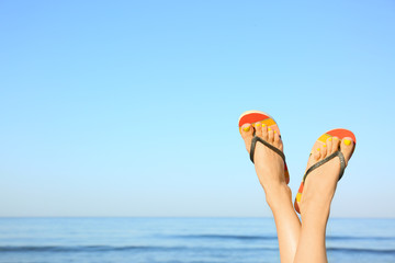 Closeup of woman wearing flip flops near sea, space for text. Beach accessories