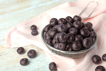 Metal sieve of fresh acai berries on light wooden table, closeup. Space for text