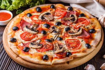 Pizza with tomato, olives, champignons, ham and cheese on round wooden plate