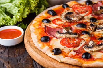 Pizza with tomato, olives, champignons, ham and cheese on round wooden plate