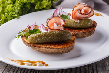 Halves baked potato with pickled cucumber, dill, salo and onion on wooden table