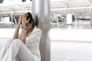 Frustrated stressed young Asian business woman with hands on face sitting at outdoors.