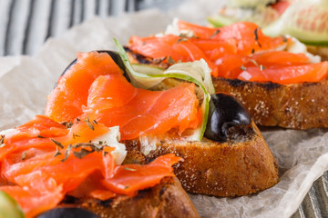 Bruschetta with smoked salmon, fresh cucumber, black olives and camembert on crumpled baking paper