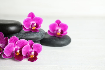 Fototapeta na wymiar Spa stones and orchid flowers on white wooden table, space for text