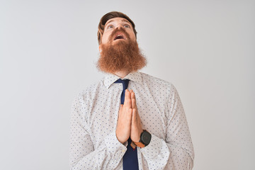 Young redhead irish businessman standing over isolated white background begging and praying with...