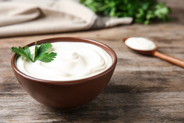 Bowl of fresh sour cream with parsley on wooden table
