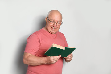 Portrait of senior man with glasses reading book on light background. Space for text