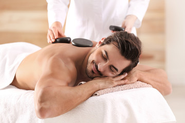 Obraz na płótnie Canvas Handsome young man receiving hot stone massage in spa salon