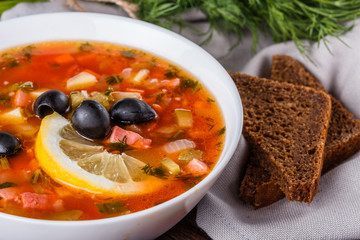 Traditional Russian meat soup Solyanka in bowl on rustic wooden table