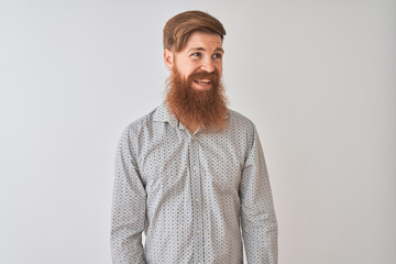 Young redhead irish man wearing casual shirt standing over isolated white background looking away to side with smile on face, natural expression. Laughing confident.