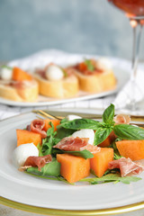 Fresh melon with prosciutto, mozzarella and basil on plate, closeup