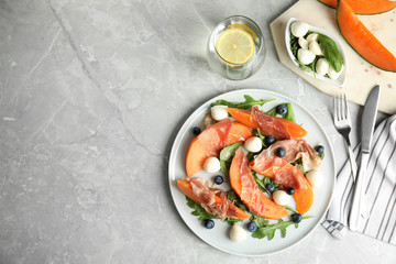 Flat lay composition of fresh melon with prosciutto on light grey marble table. Space for text