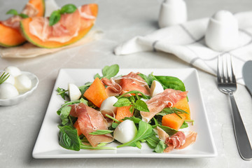 Fresh melon with prosciutto, mozzarella and arugula on table