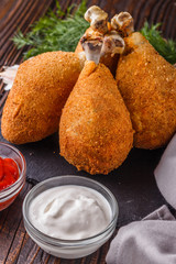 fried chicken leg in batter, red and white sauce on a dark surface