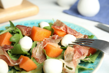 Fresh melon with prosciutto, mozzarella and arugula on plate, closeup