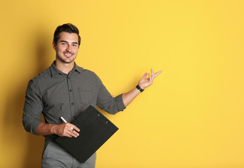 Young male teacher with clipboard on yellow background. Space for text