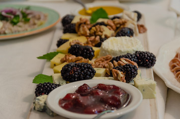 Wooden board with different types of cheese, walnuts, blackberries, strawberry jam and honey. Restaurant serving