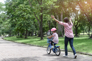Mother teaching her daughter riding bicycle.Little girl wearing safety equipment. 