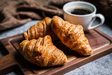 Breakfast with fresh croissants and cup of black coffee on wooden board