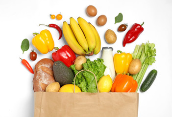 Shopping paper bag with different groceries on white background, top view