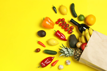 Shopping paper bag with different groceries on yellow background, flat lay. Space for text
