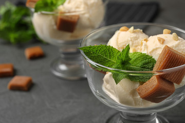 Glass bowl of ice cream with caramel candies and mint on grey table, closeup