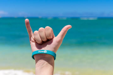 Hawaiian shaka sign. Hang Loose sign, being made with a blue sky and tropical sea in the background.  