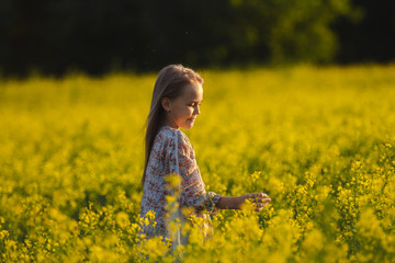 Naklejka na ściany i meble The concept of health and youth. Carefree young girl enjoys the sunset in a canola field.