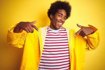 African american man with afro hair wearing rain coat standing over isolated yellow background...