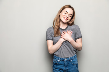 Carefree woman in stylish spectacles friendly smiling and hands on heart sign while standing against beige background