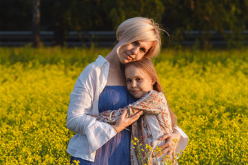 The concept of parenting. Beautiful mother and daughter on a yellow rape field