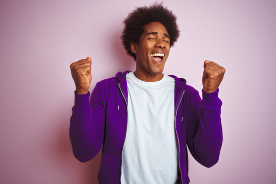 Young african american man wearing purple sweatshirt standing over isolated pink background celebrating surprised and amazed for success with arms raised and eyes closed. Winner concept.