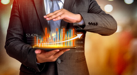 Business people hold a tablet, plan and strategy and display virtual holograms of statistics, financial graphs, securities and charts on a dark background. The concept of business growth