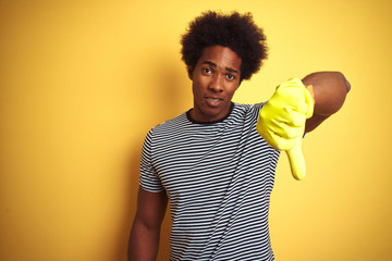 Young african american man cleaning using gloves standing over isolated yellow background with...