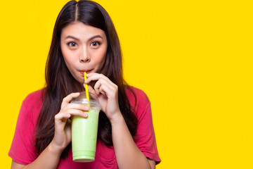 Beautiful asian woman drink iced green tea, make her refreshing in summer season. Attractive beautiful girl use straw for drinking iced green tea. She hold plastic glass. yellow background, copy space