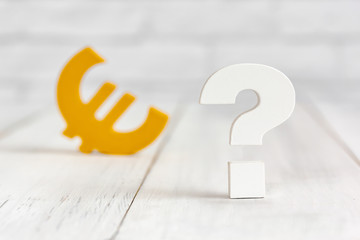 Question mark with euro sign on white wood table over white brick background with copy space.