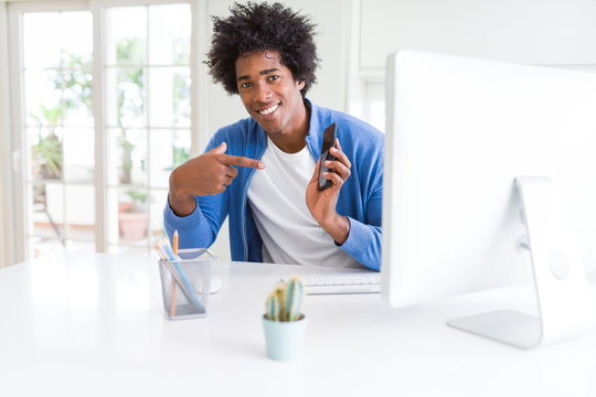 African American man working using smartphone and computer very happy pointing with hand and finger