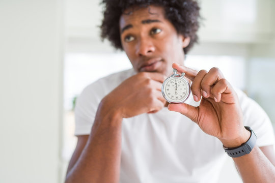 African American man holding stopwatch serious face thinking about question, very confused idea