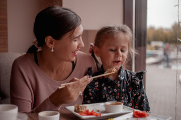 A woman is feeding her daughter a sushi of traditional Japanese food