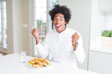 Fototapeta na wymiar African American hungry man eating hamburger for lunch celebrating surprised and amazed for success with arms raised and open eyes. Winner concept.
