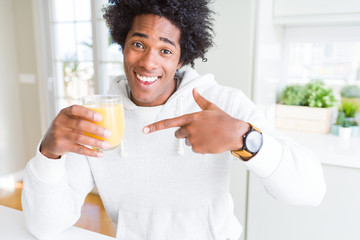African American man holding and drinking glass of orange juice very happy pointing with hand and...