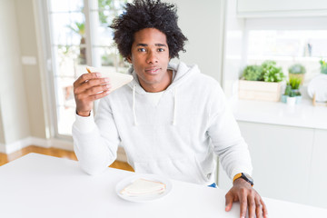 Fototapeta na wymiar African American man eating handmade sandwich at home with a confident expression on smart face thinking serious