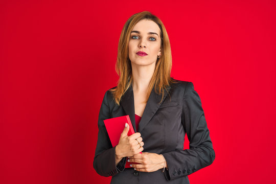 Young beautiful redhead businesswoman wearing suit holding book