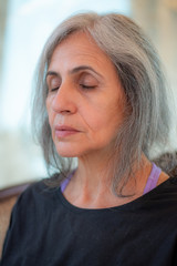 Senior Indian woman with grey hair and glowing skin, meditating in the morning. 