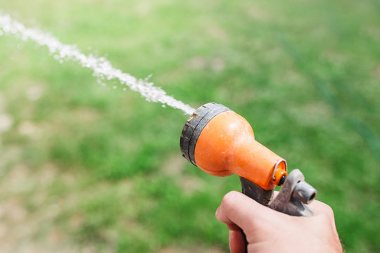 Closeup hand of a Caucasian man with a nozzle spray on a garden hose and a stream of water from it - watering