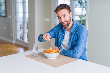 Handsome man eating pasta with meatballs and tomato sauce at home while smiling at the camera